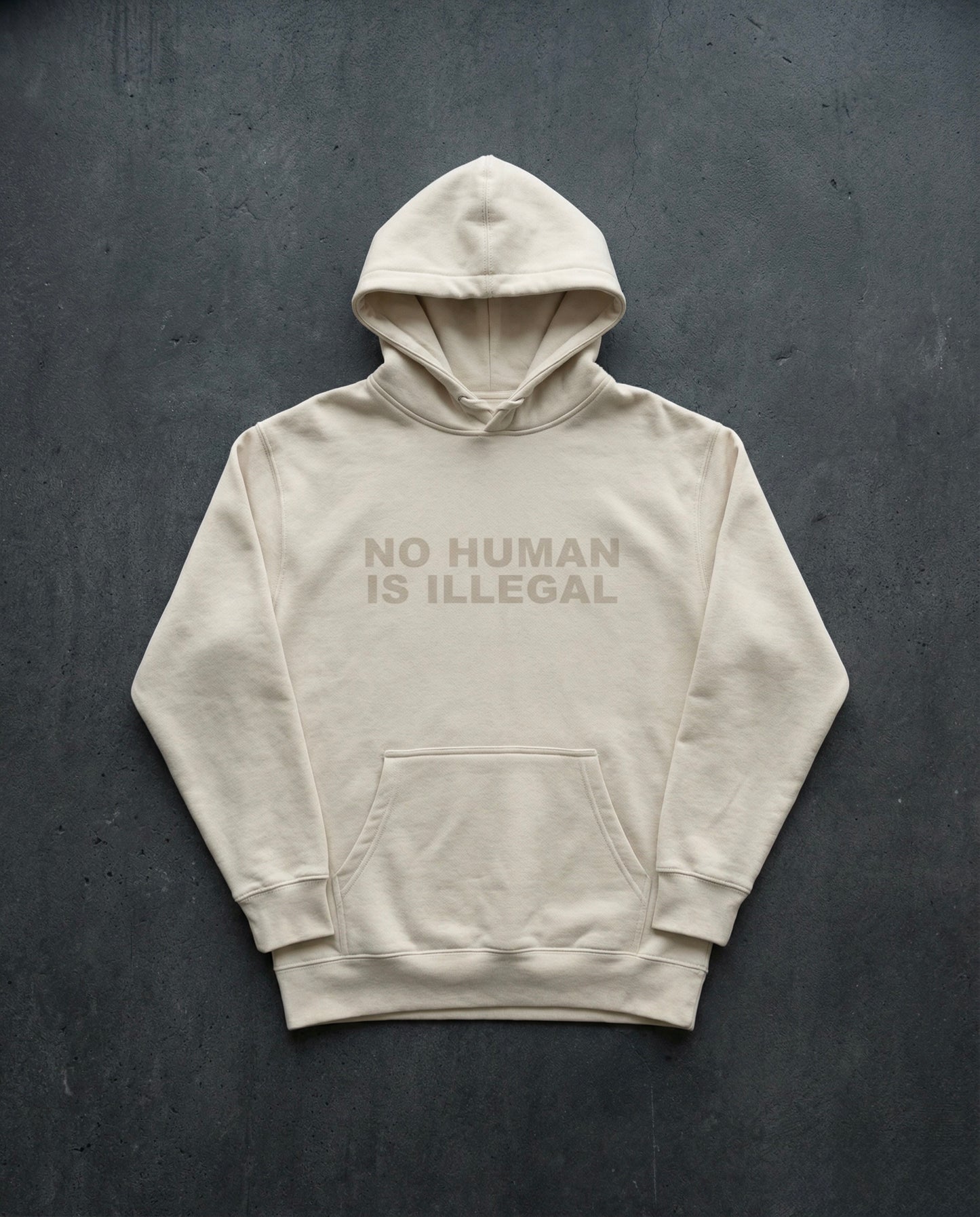 NO HUMAN IS ILLEGAL Shadow Edition Hoodie concrete background in bone | BAD BUREAU