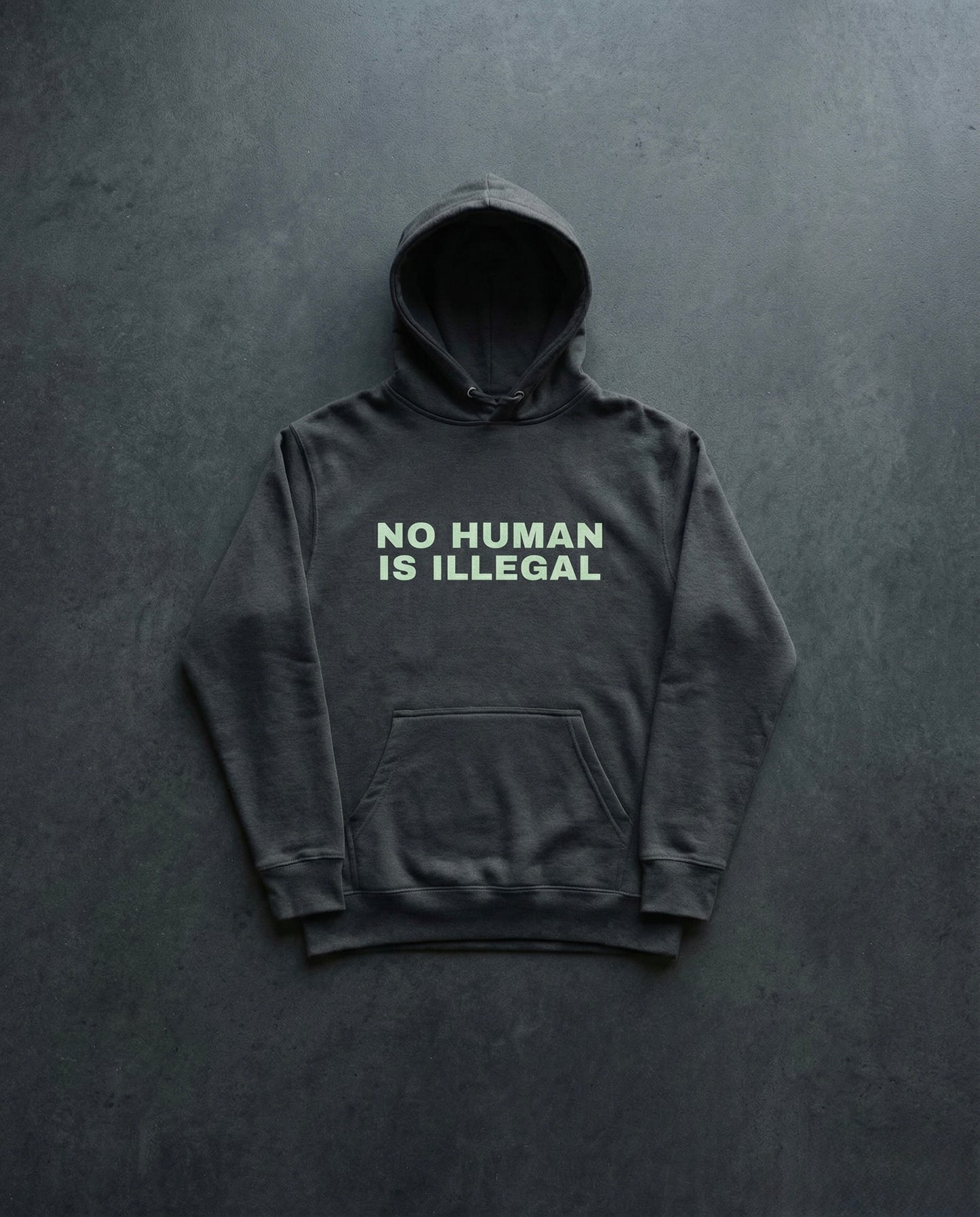 NO HUMAN IS ILLEGAL Hoodie Concrete Background in Charcoal | BAD BUREAU 