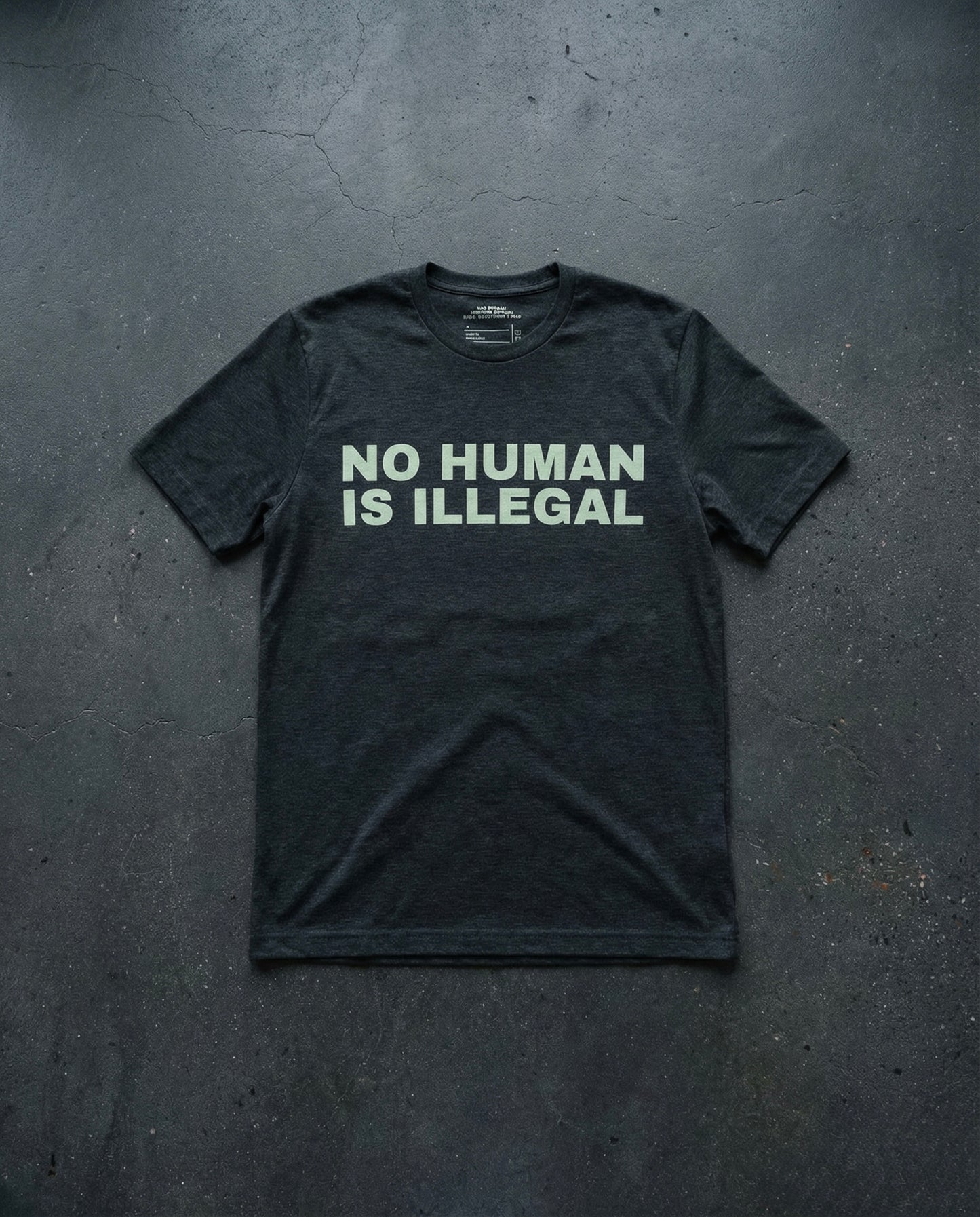 NO HUMAN IS ILLEGAL T-Shirt Concrete Background in Charcoal | BAD BUREAU 