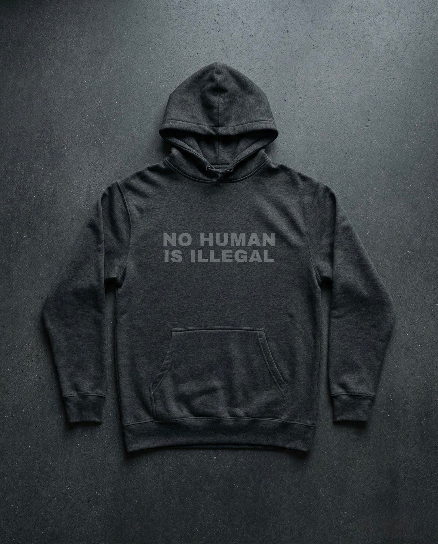 NO HUMAN IS ILLEGAL Shadow Edition Hoodie concrete background in charcoal | BAD BUREAU 