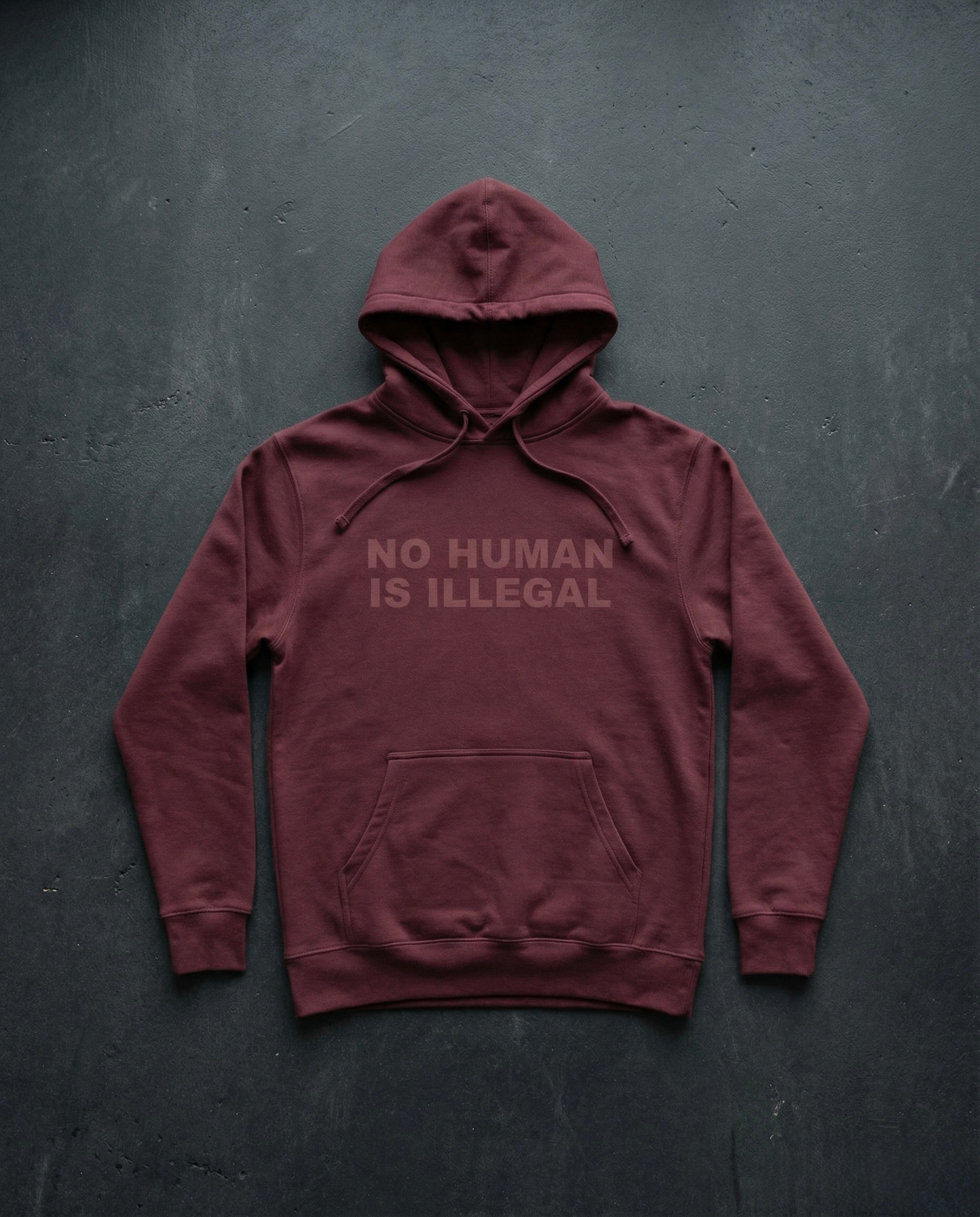 NO HUMAN IS ILLEGAL Shadow Edition Hoodie concrete background in maroon | BAD BUREAU 